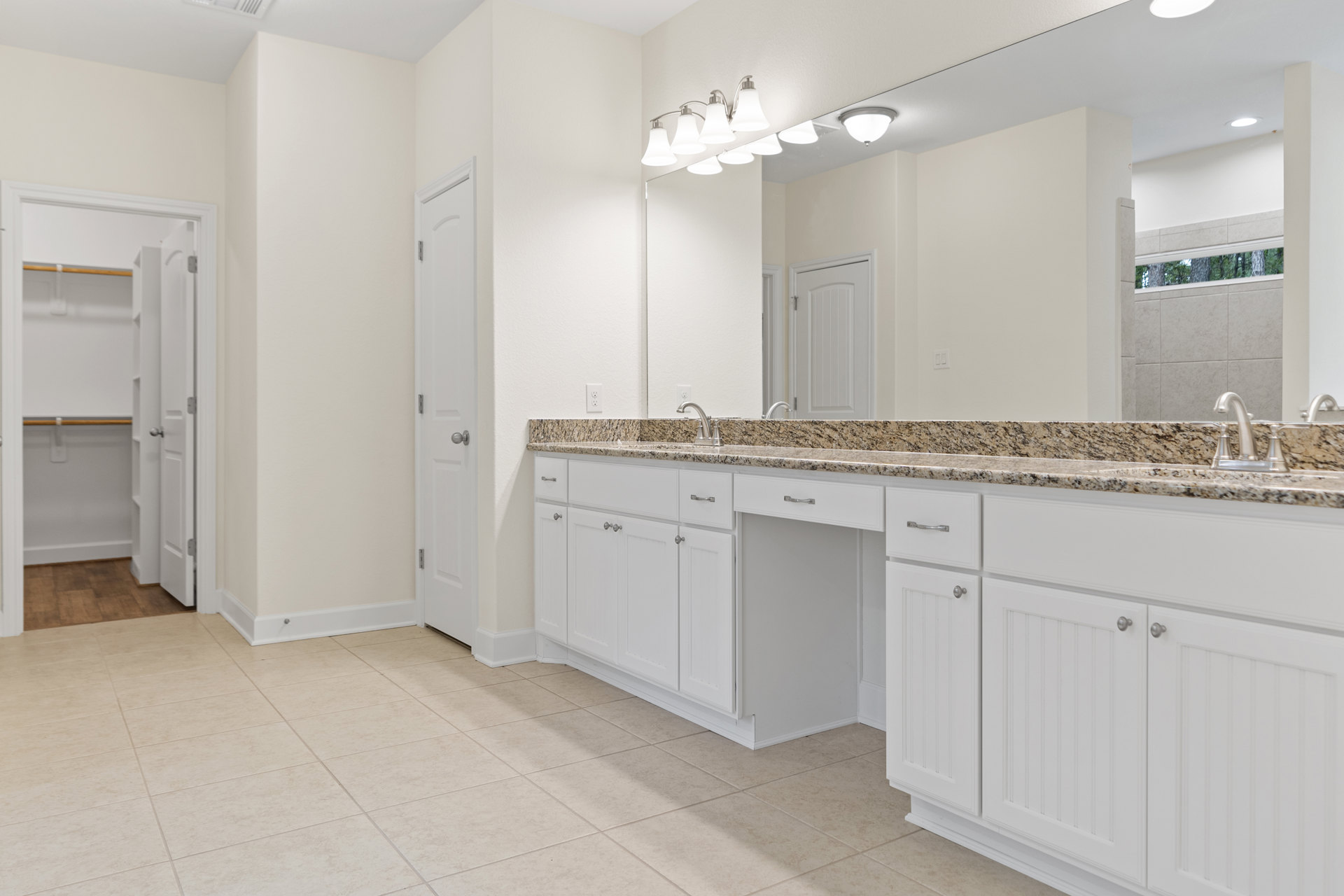 Bathroom with marble countertop, undermount sink, large framed mirror, white cabinetry, chrome faucet, and tile flooring