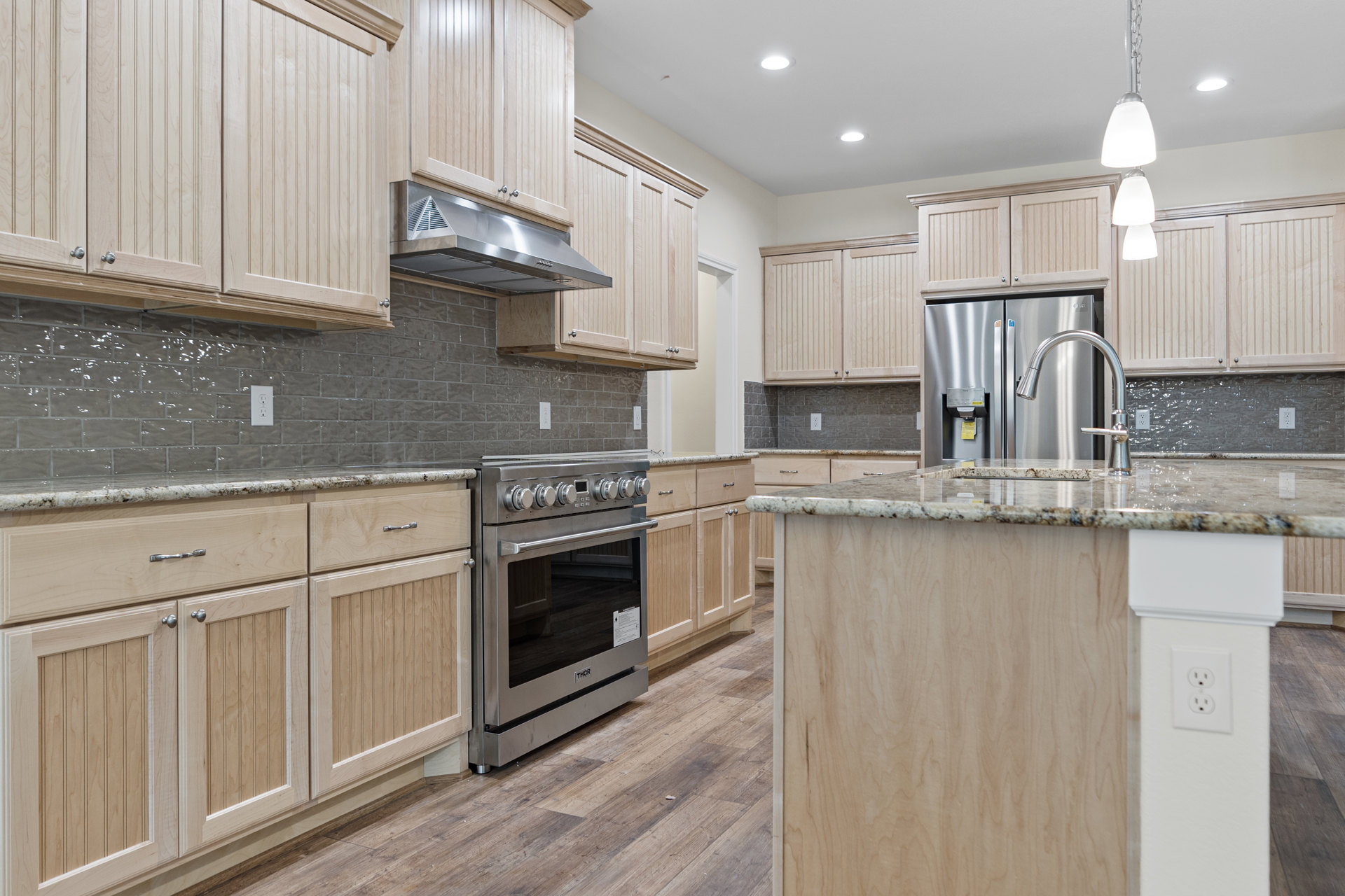 Kitchen featuring wood cabinetry, stainless steel stove with open oven door, stainless steel refrigerator, silver faucet, and range hood.