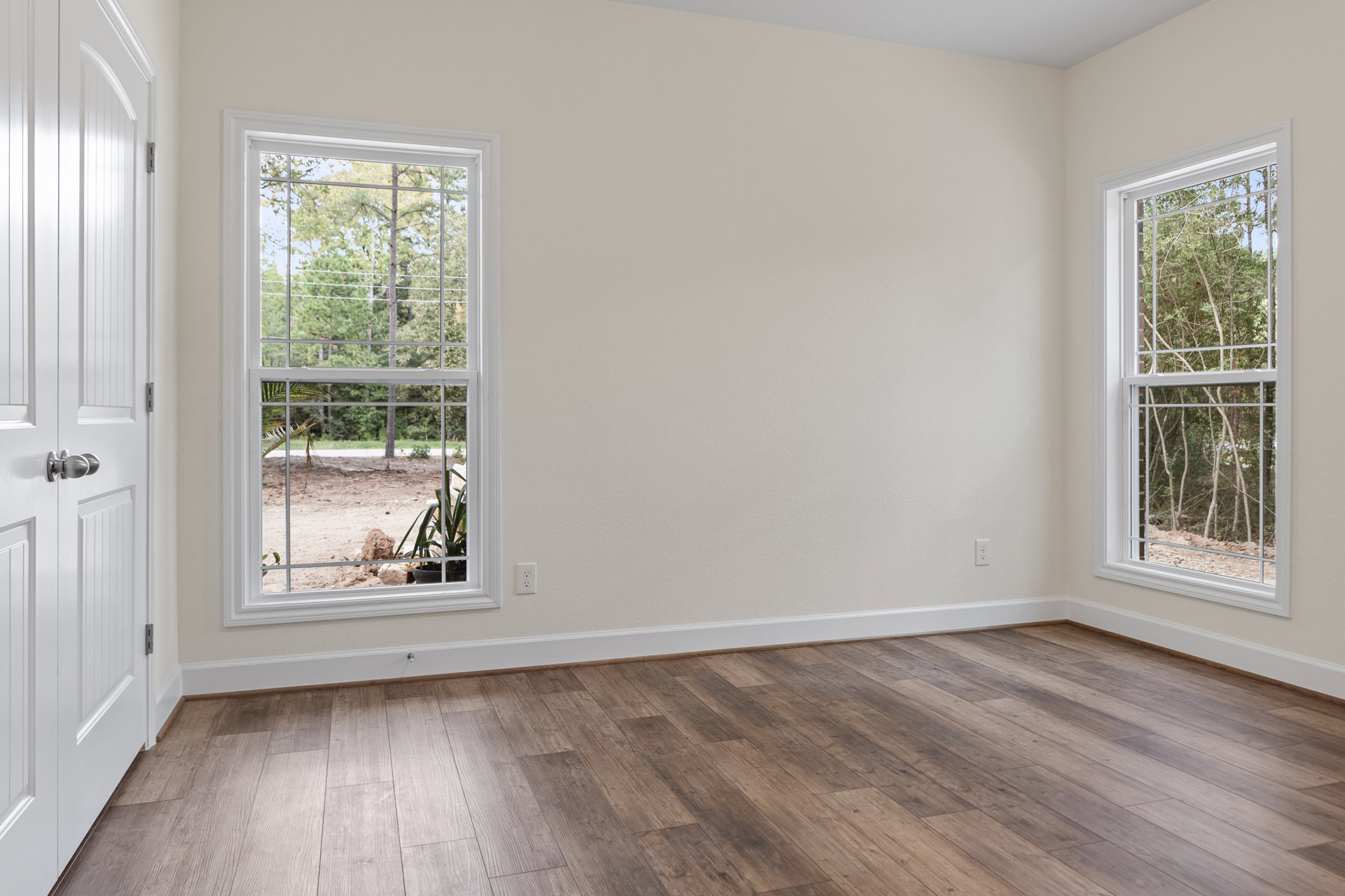 Hardwood flooring with white baseboards, large window overlooking trees, white walls, and a door with a round knob