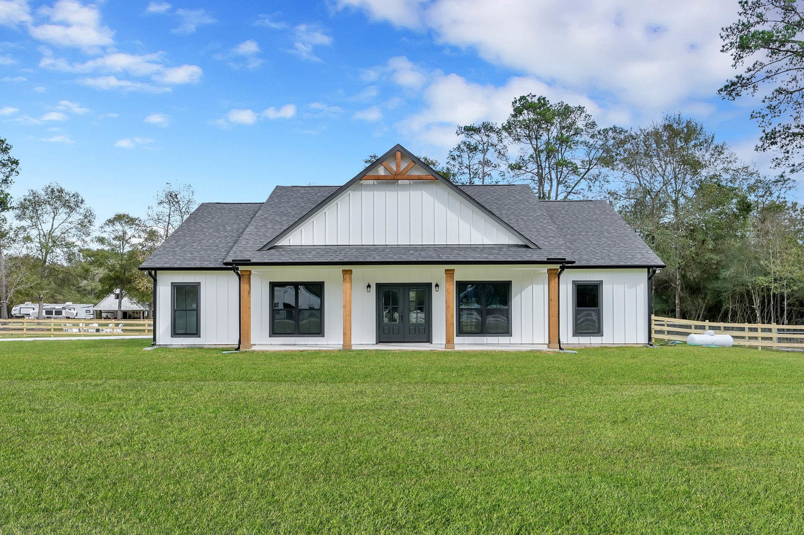 White house with black roof and double black doors, surrounded by green lawn, trees, and cloudy sky in the background