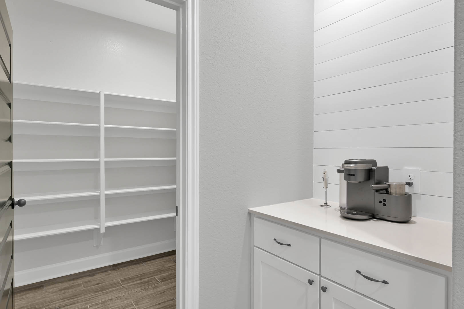 White kitchen with open white shelves, light wood flooring, white baseboards, stainless steel coffee machine on countertop, close-up of shelving and appliances