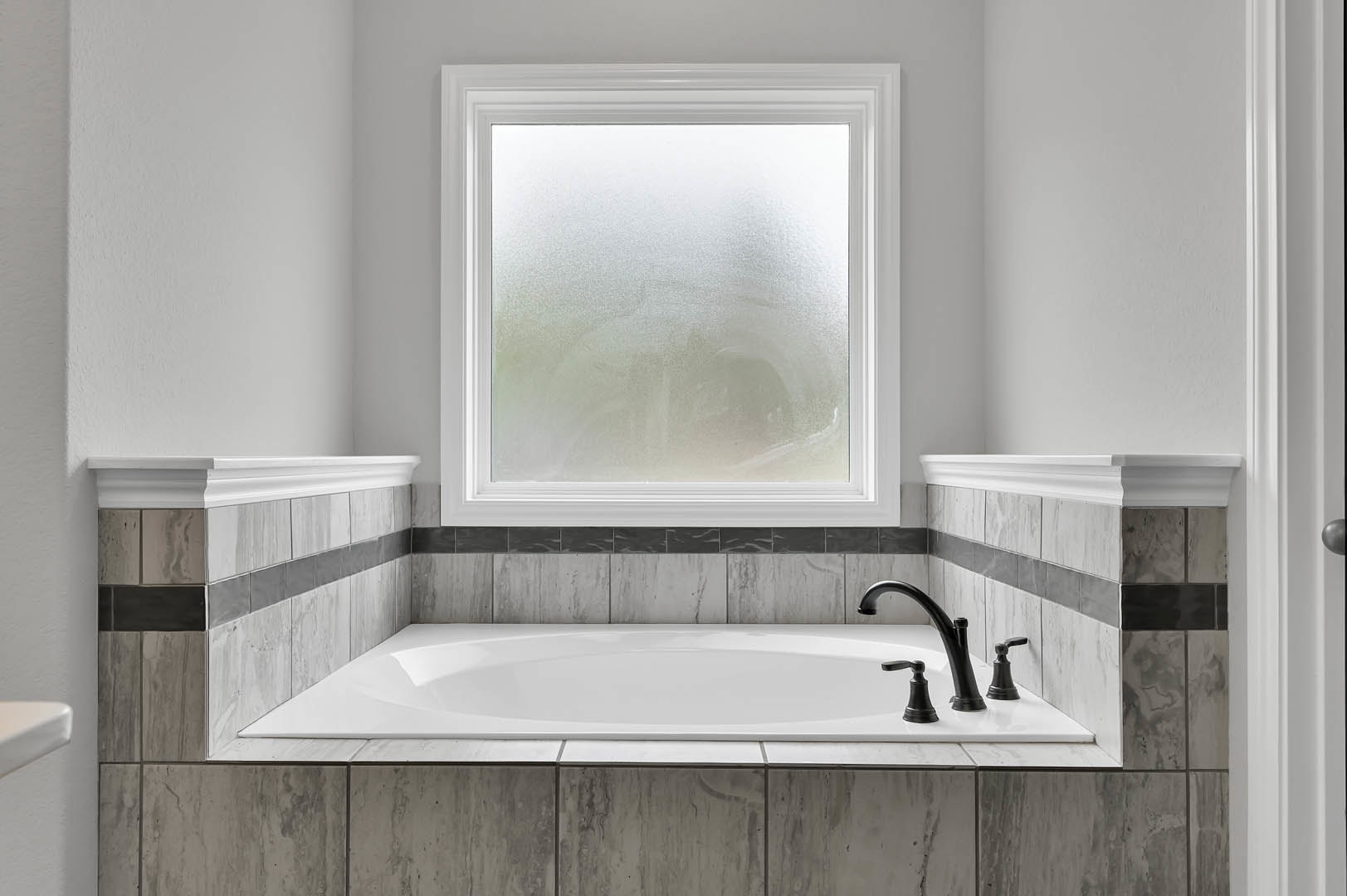 White freestanding bathtub with silver faucet and handle, frosted glass window above, white tile wall and baseboard