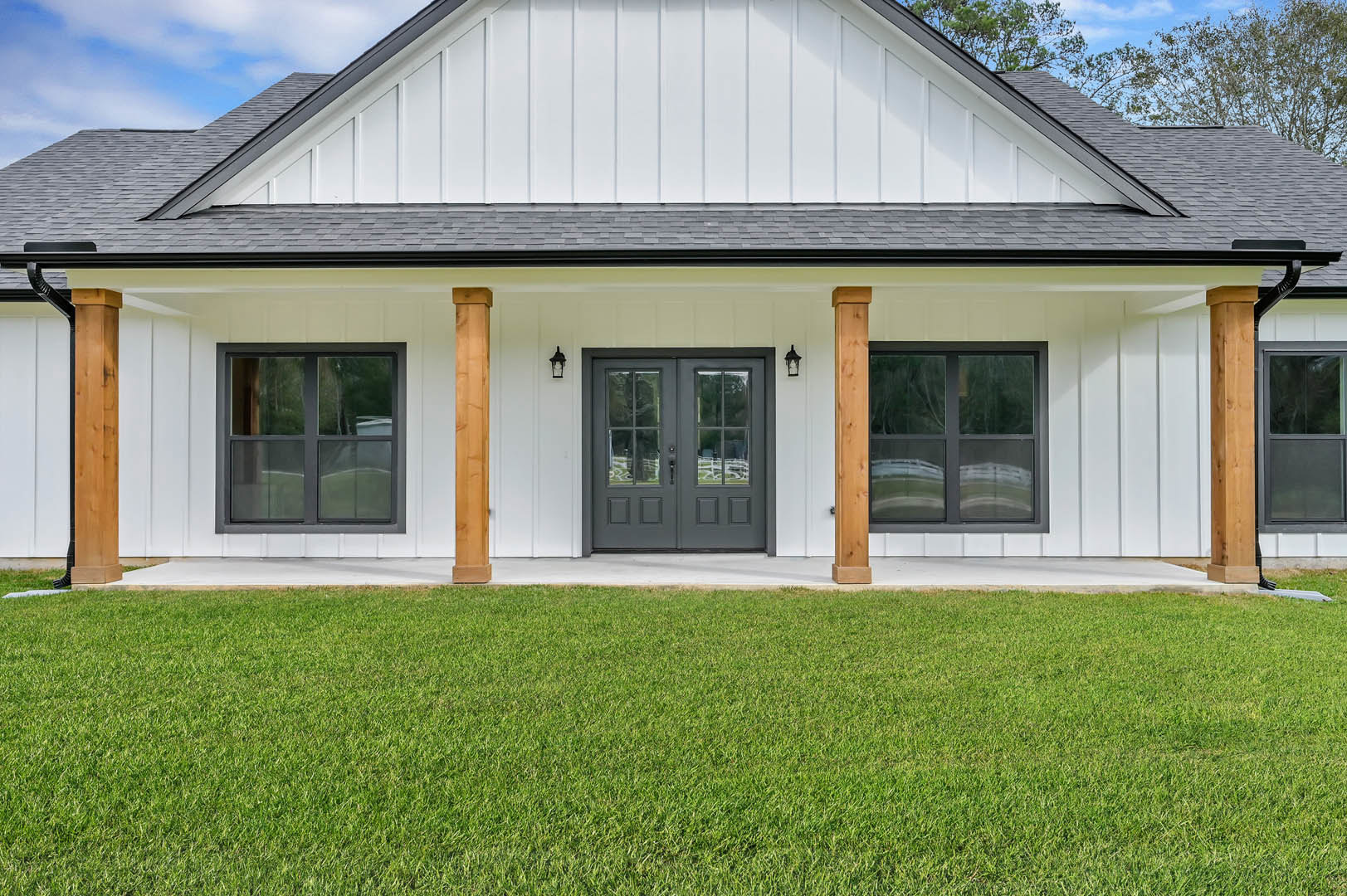 White two-story house with glass-paneled double doors, gray accents, large windows, wooden paneling, and manicured green lawn