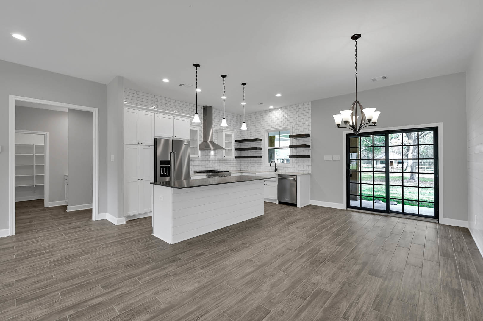 Open kitchen and dining area with wood flooring, white cabinetry, black countertops, sliding glass door overlooking yard, refrigerator, white walls, closet door, and ceiling