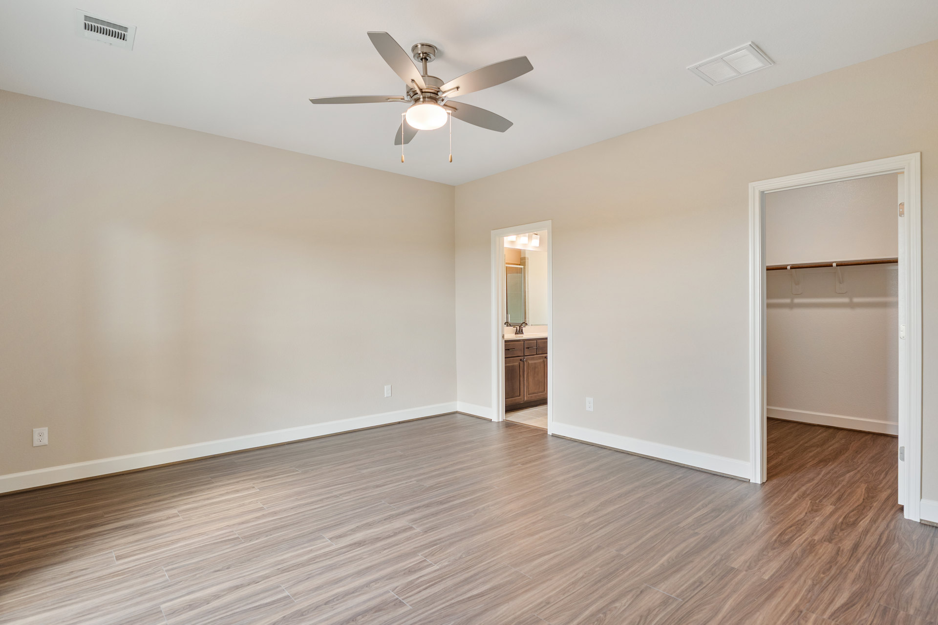 Ceiling fan with light fixture, hardwood flooring, open door leading to closet with wooden rail, white ceiling vent, neutral walls
