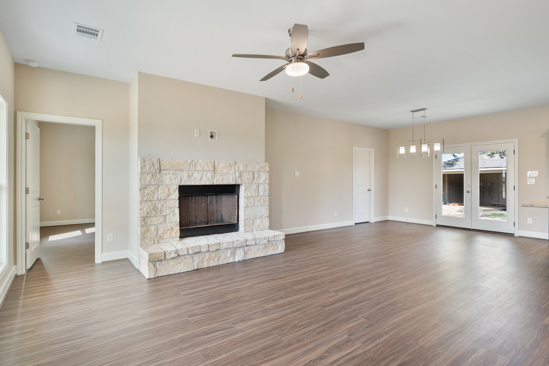 Living room with wood flooring, central fireplace with mesh screen, ceiling fan with light, and double glass-paneled doors