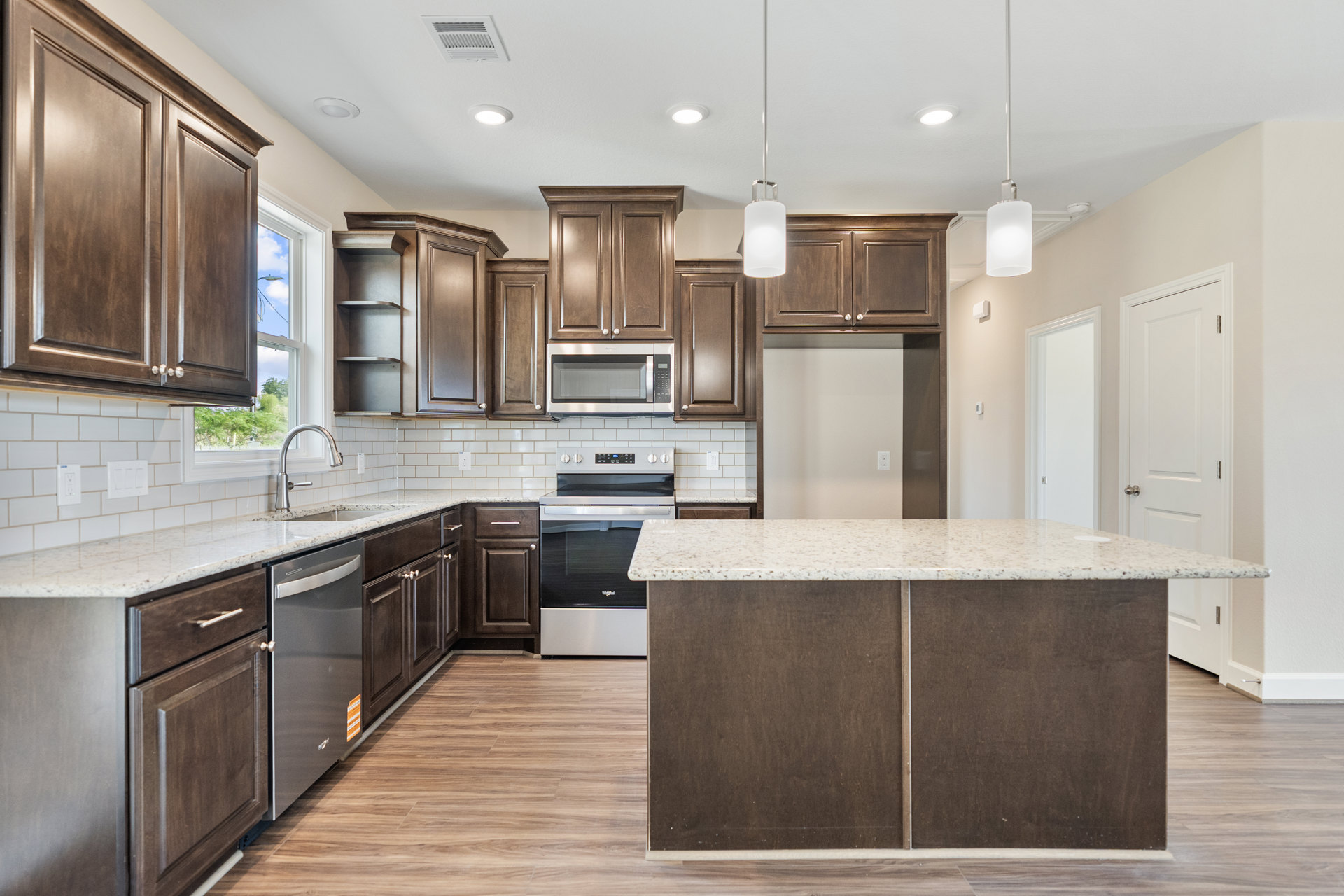 Dark wood kitchen cabinets with sleek white marble countertops, stainless steel oven and microwave, metal cabinet door, towel draped over microwave, modern light switch on wall