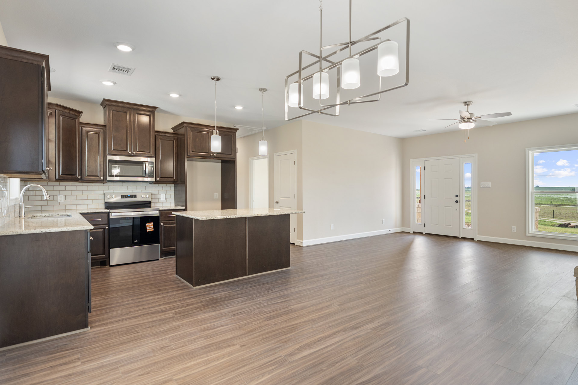 Open kitchen and dining area with wood laminate flooring, white walls, brown cabinetry, stainless steel stove with sticker on oven glass, built-in microwave, sink, and window