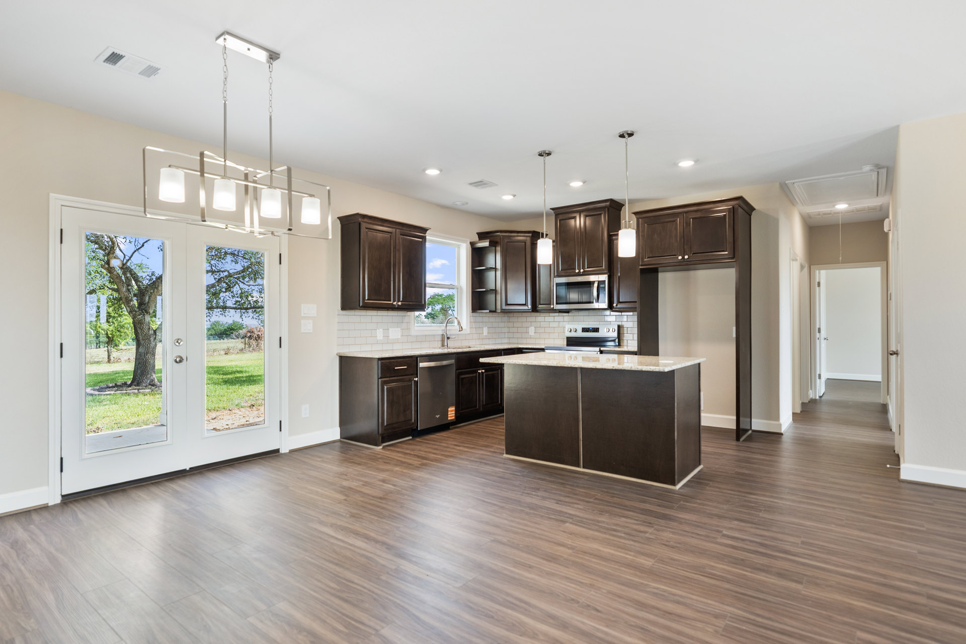 Kitchen with dark wood cabinets, wood plank flooring, stone countertop, built-in microwave, and large window with tree view