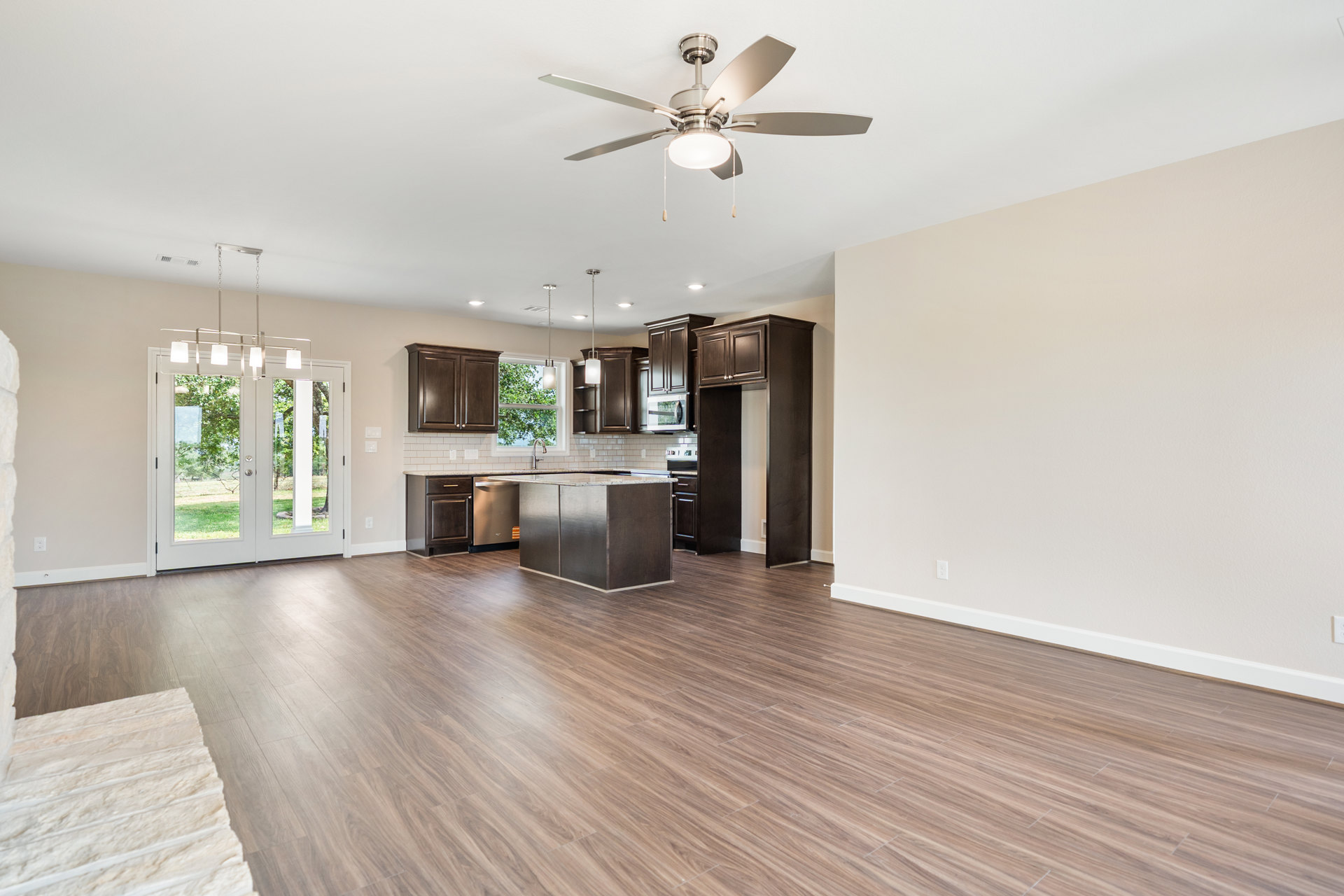 Open kitchen and living room featuring wood flooring, marble-topped kitchen island, ceiling fan with light, built-in microwave, and white double doors with glass panels.