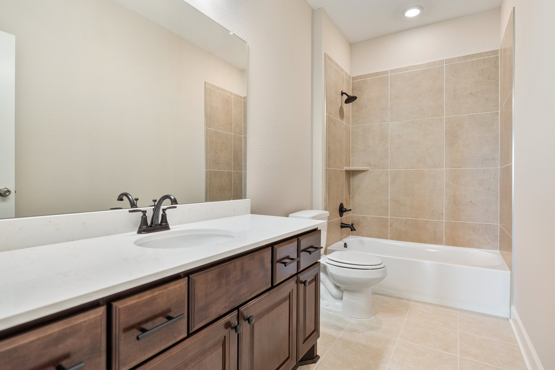 Modern bathroom featuring a white toilet with closed seat, rectangular sink set into a light-colored countertop, chrome faucet, and tile walls; partial view of bathtub and