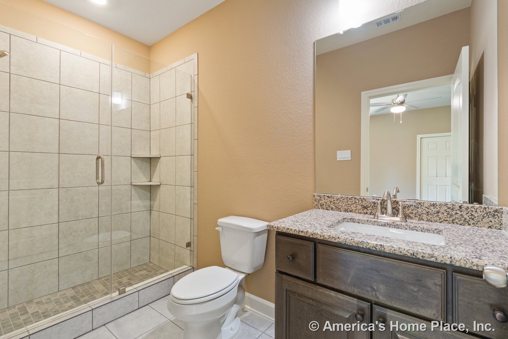 Glass-enclosed shower with large beige wall tiles, granite vanity countertop atop dark wood cabinetry, recessed ceiling light, rectangular wall mirror, built-in shelves, and tiled