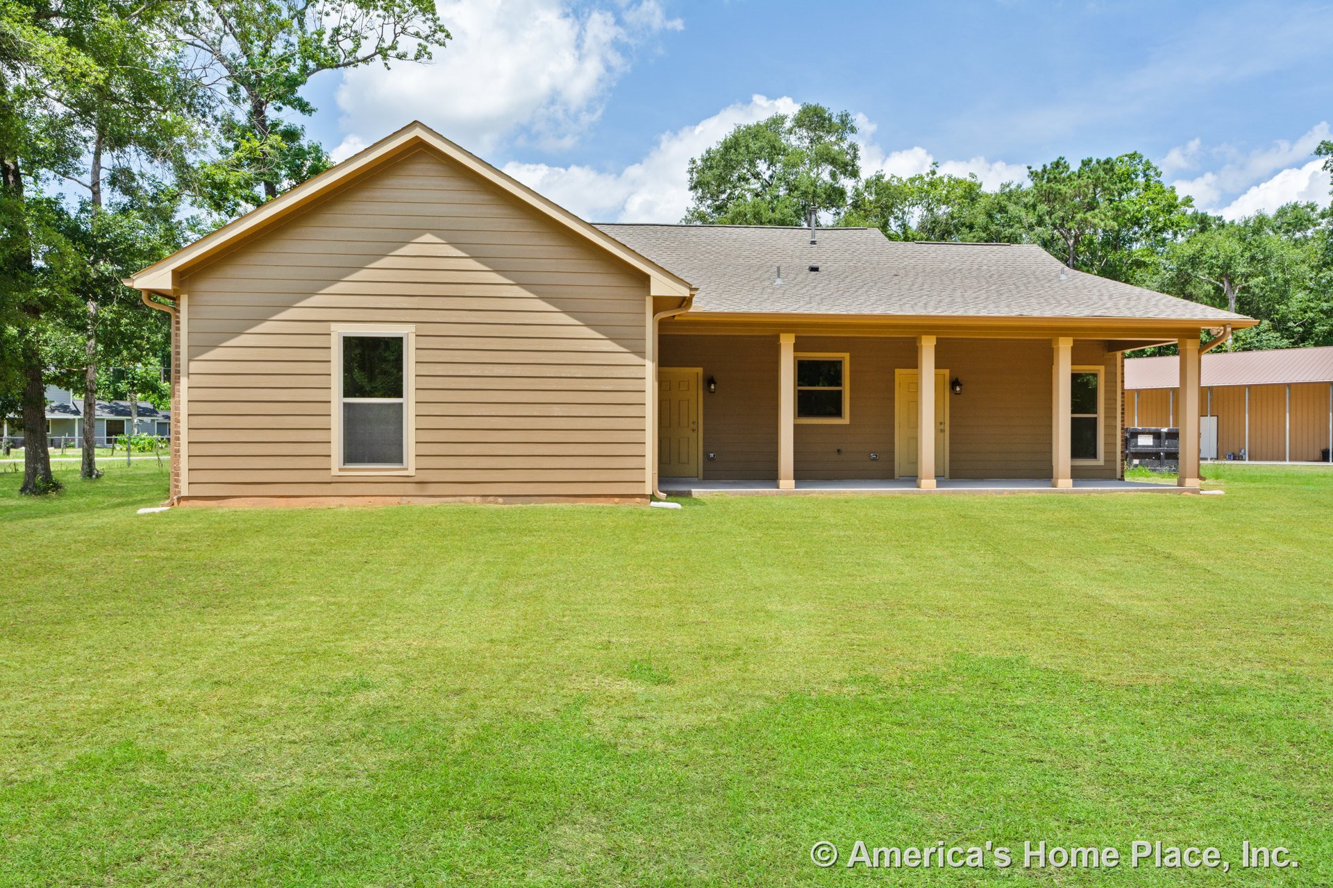 Covered back porch with four white columns, tan horizontal siding, single window, two exterior doors, shingled roof, exterior lighting fixture, and landscaped yard.