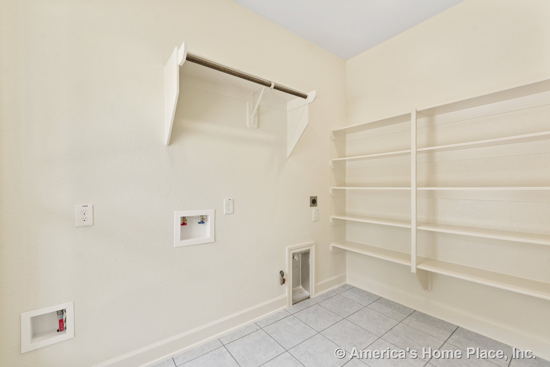 Laundry room with wall-mounted open shelving, hanging rod for garments, tile flooring, utility hookups, multiple wall outlets, light-colored walls, and baseboard trim.