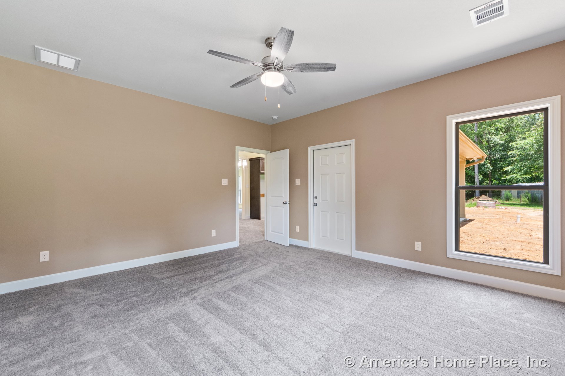Bedroom with light gray carpet, beige painted walls, large window with white trim, white baseboards, ceiling fan with built-in light, and two-panel interior doors.