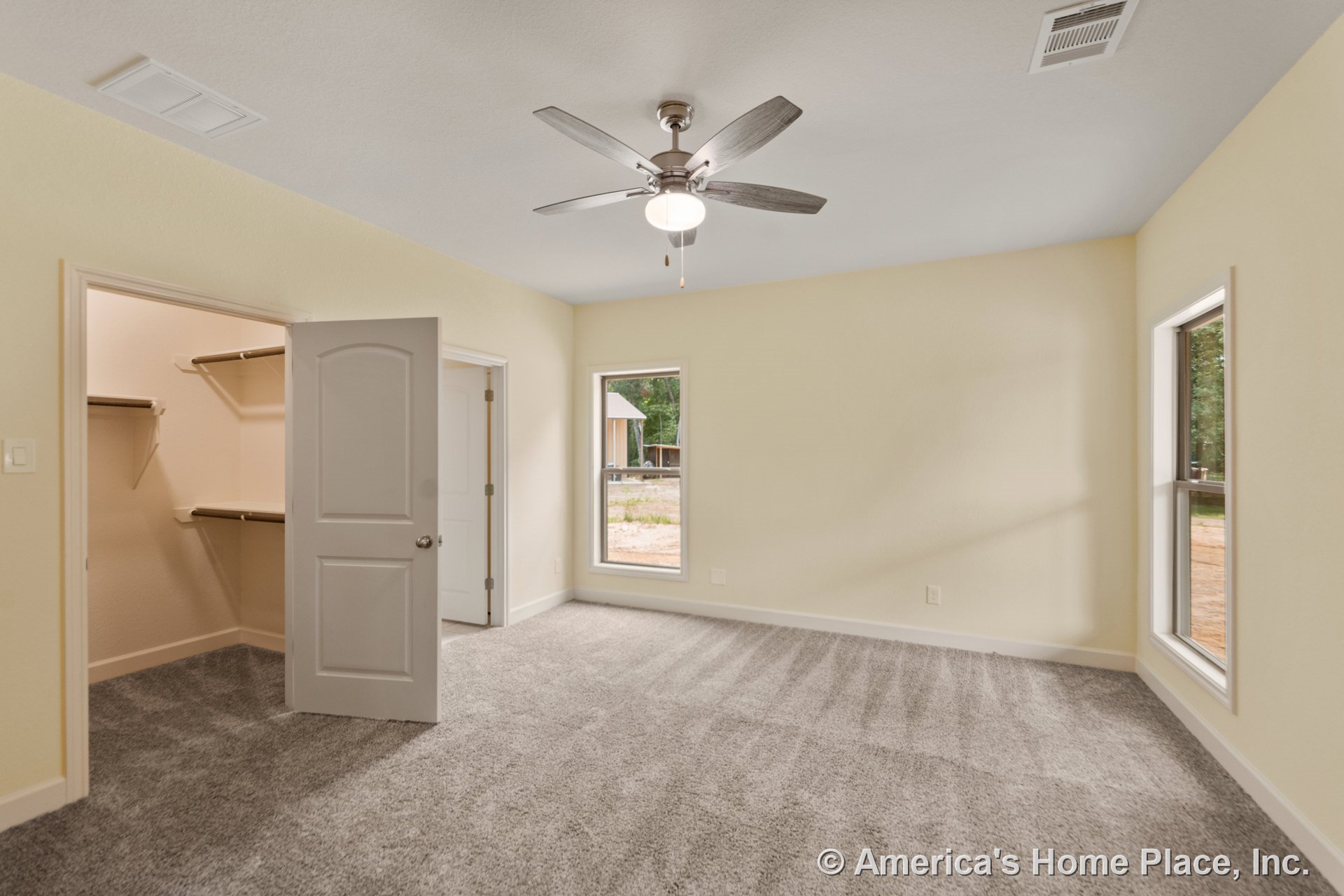 Bedroom with gray carpet flooring, two rectangular windows, ceiling fan with integrated light, open walk-in closet featuring built-in shelving, neutral walls, white trim and