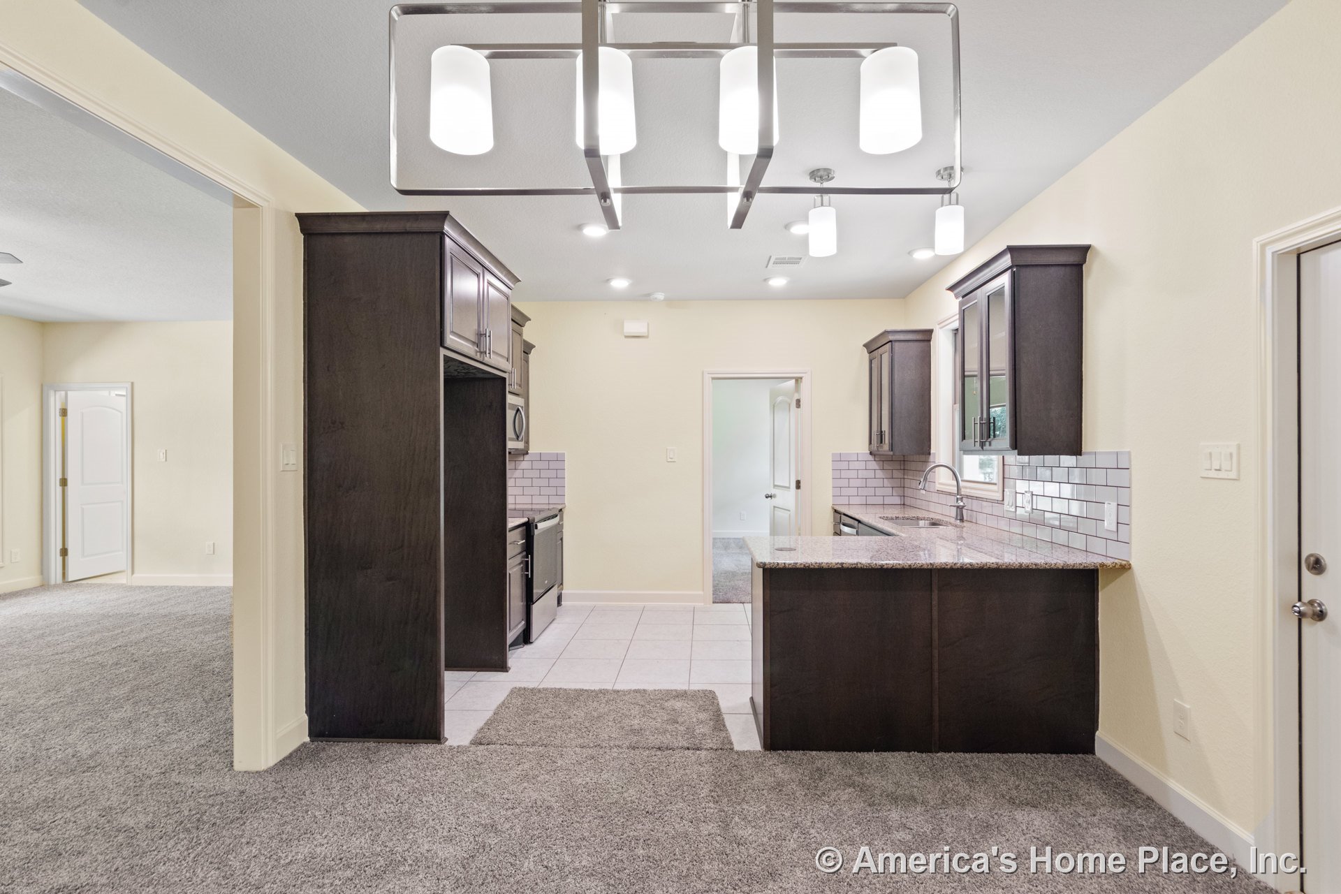 Dark wood kitchen cabinetry with granite countertop peninsula, white subway tile backsplash, built-in stainless sink beneath window, tile flooring, recessed and pendant ceiling