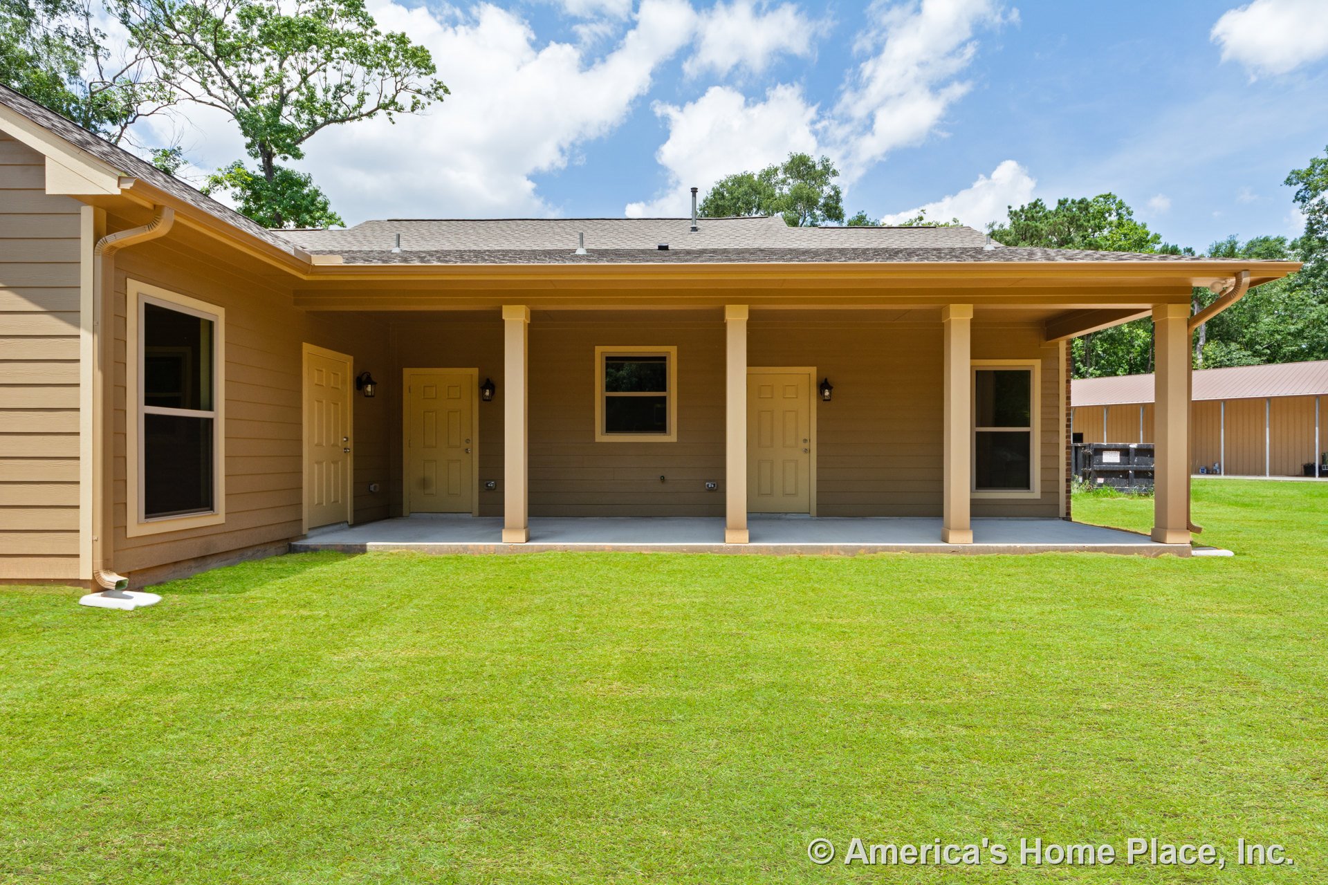 Covered back porch with three entry doors, tan horizontal siding, concrete patio floor, rectangular windows, exterior wall-mounted lights, white trim, supporting columns, and