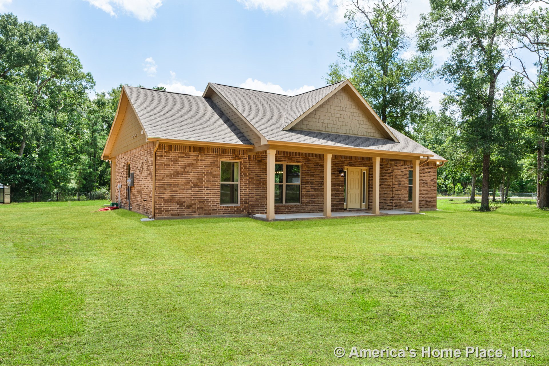 Brick exterior with gable roof, covered front porch supported by trimmed columns, double front windows, and central front entry door; landscaped yard in foreground.