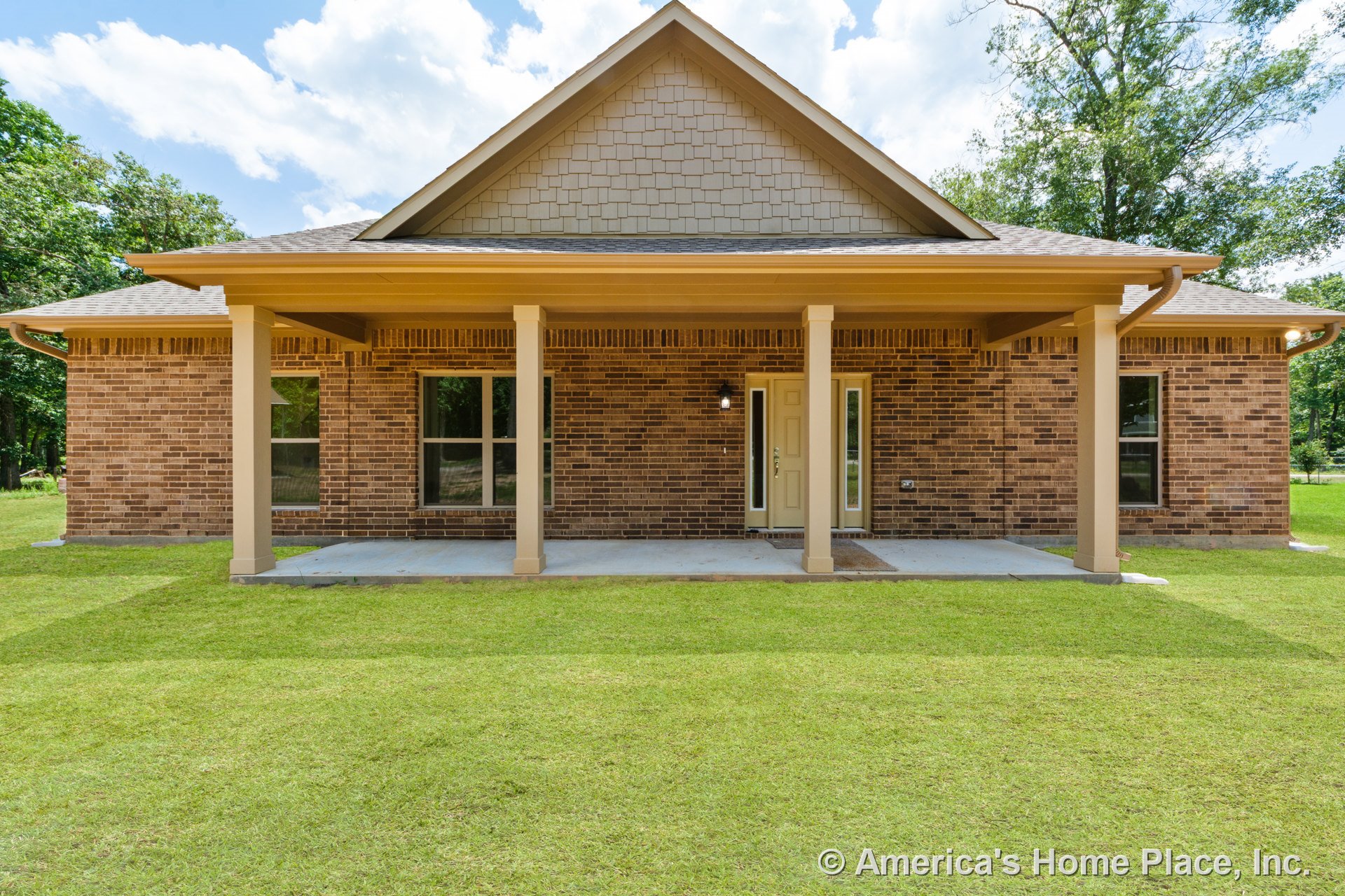 Brick exterior with covered front porch supported by two columns, double front windows, tan front door, gable roof, white trim, permanent lighting, concrete slab walkway, and