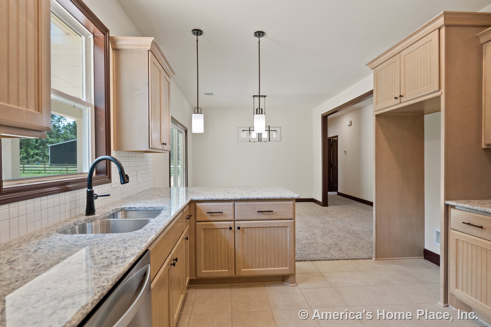Light wood cabinetry and granite countertops with a white tile backsplash, double stainless sink and faucet built into the peninsula, pendant lighting overhead, tile flooring