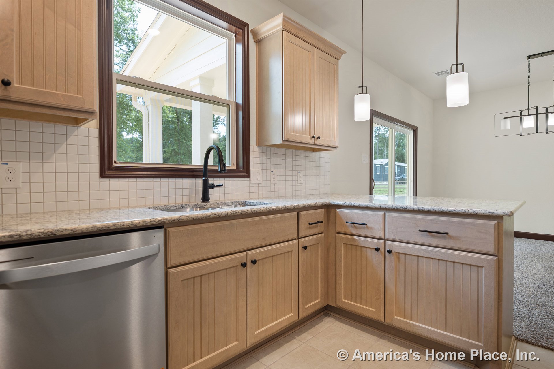 Light wood cabinetry with granite countertops, tile backsplash, stainless steel dishwasher, pendant lighting, and a large window above the sink in an open kitchen layout.
