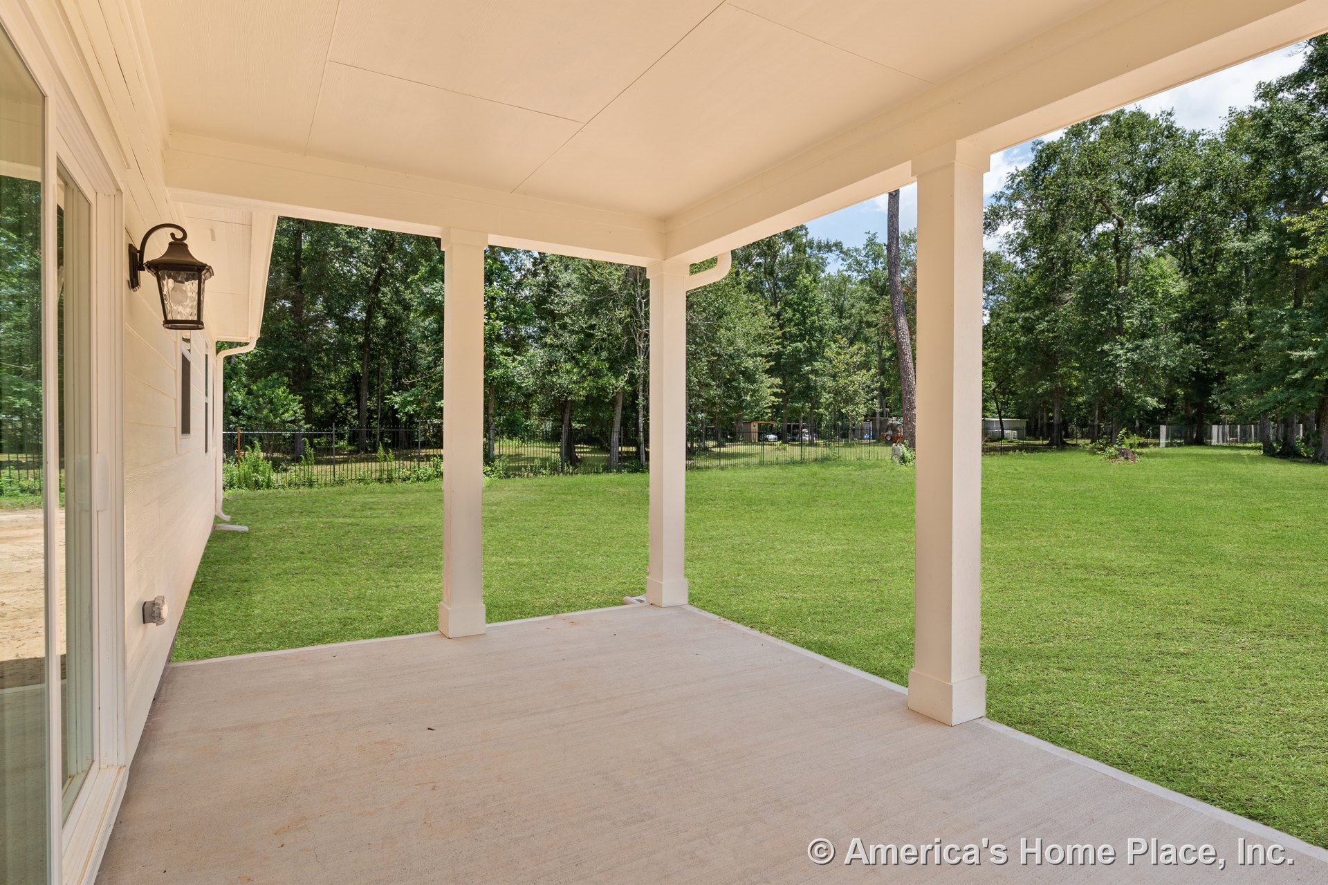 Covered back porch with concrete flooring, white trim support columns, exterior wall sconce lighting, sliding glass door, and finished ceiling.