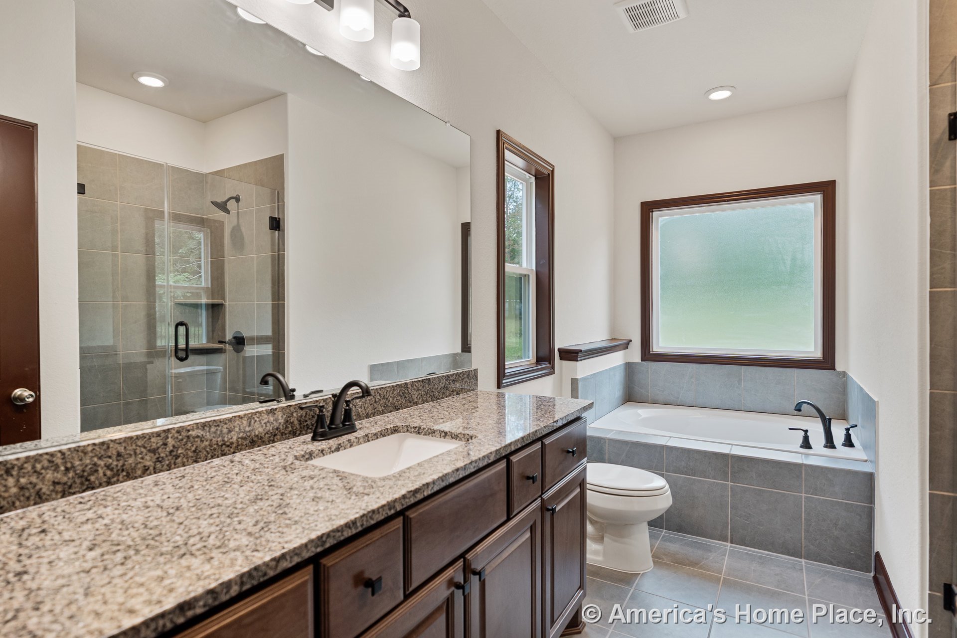 Granite countertop vanity with dark wood cabinetry, single sink, large mirror, recessed ceiling lighting, tiled walk-in shower, soaking tub with tile surround, and expansive
