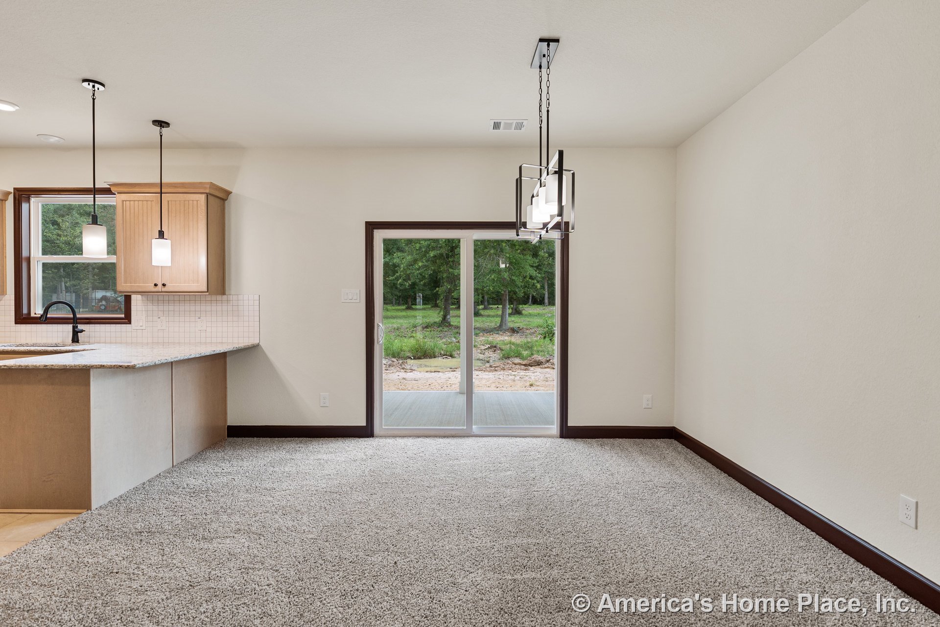 Dining area with carpet flooring, sliding glass door framed in dark trim, modern pendant lighting overhead, adjacent kitchen featuring light wood cabinetry, granite countertops