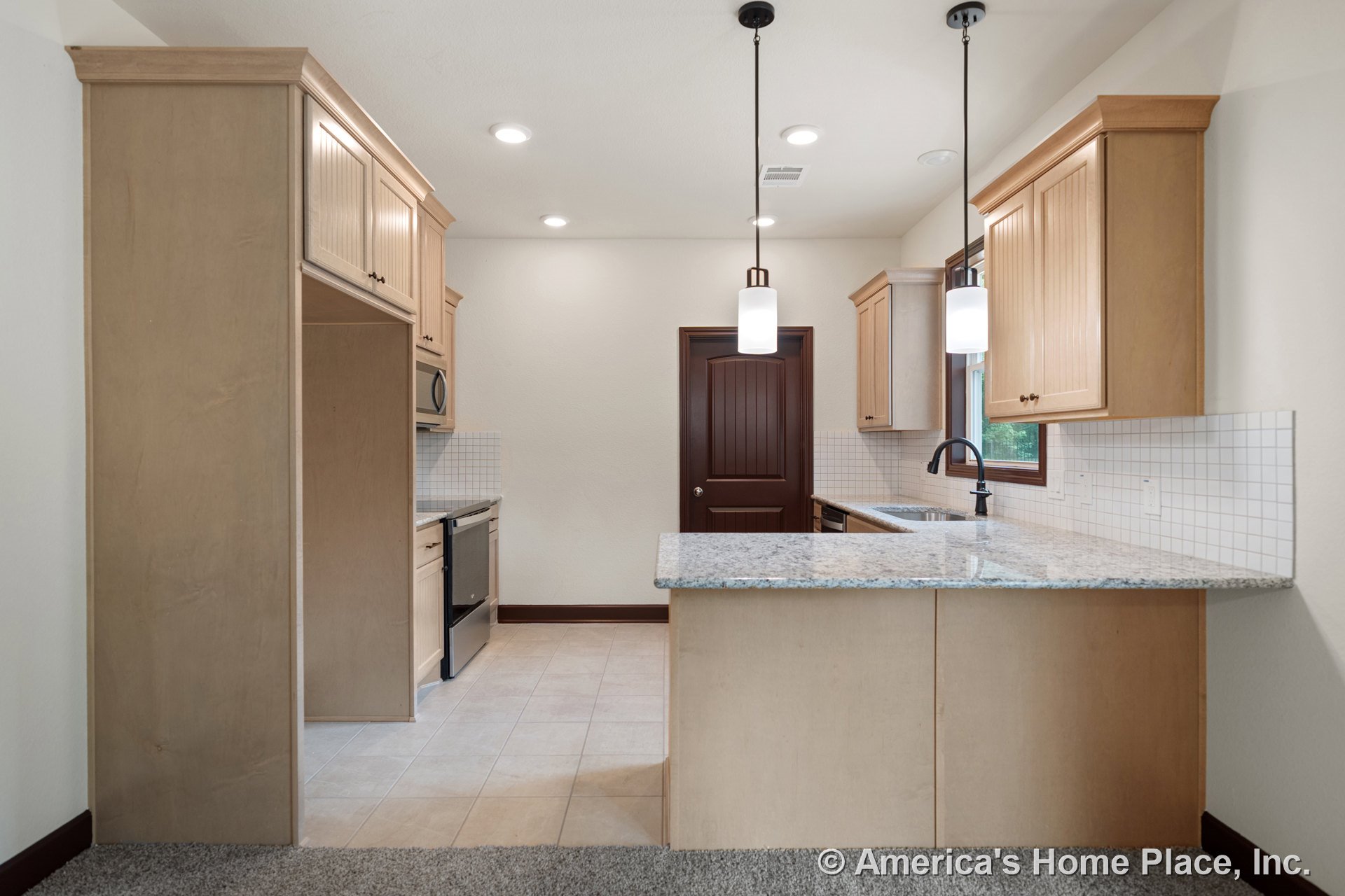 Light wood kitchen cabinetry with granite peninsula countertop, tile backsplash, and tile flooring; built-in microwave and oven; pendant lighting fixtures above workspace; window
