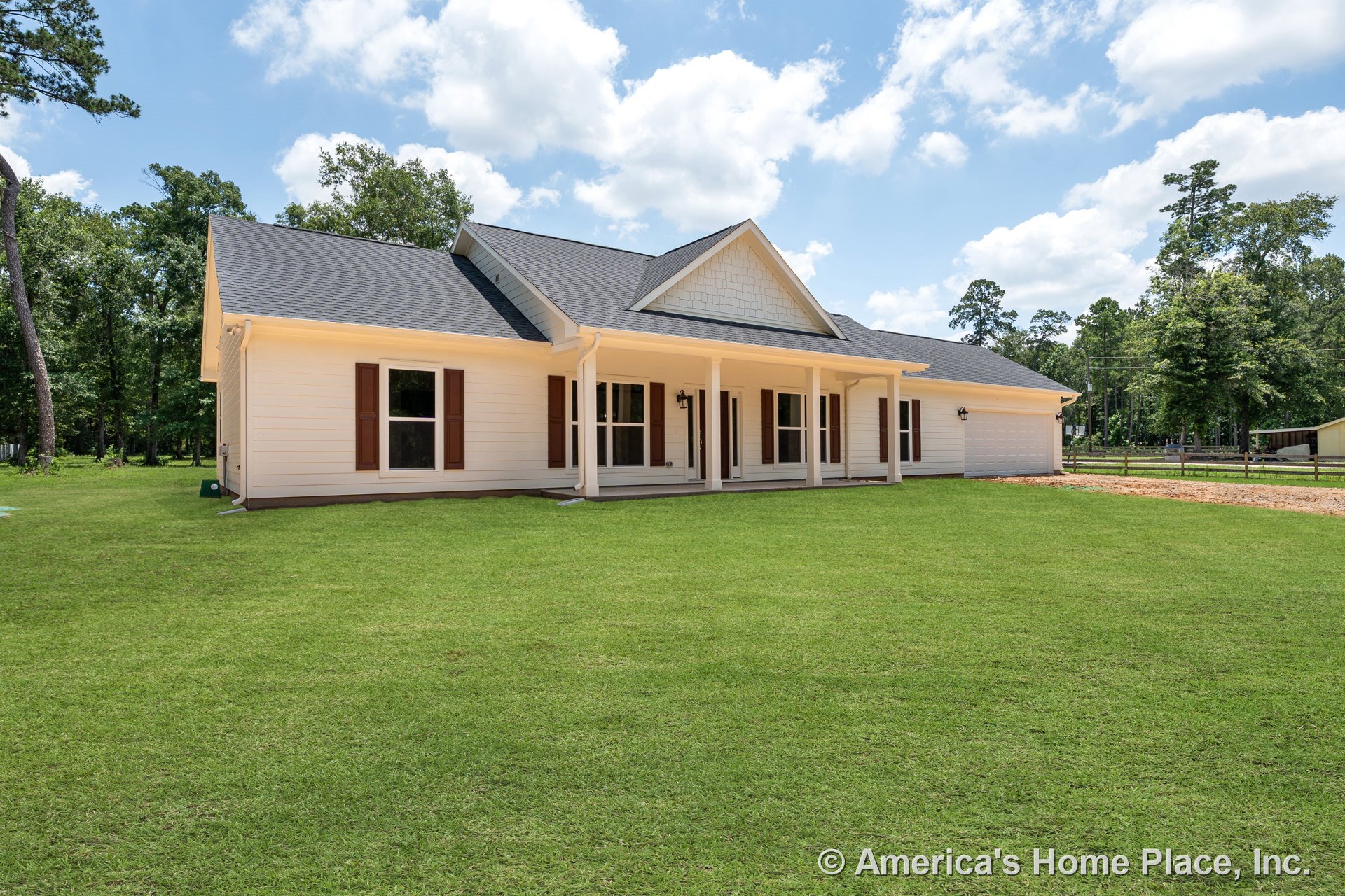 Large covered front porch with white columns, white exterior siding, multiple large windows with brown shutters, attached garage, gable roof, front entry lighting, and landscaped