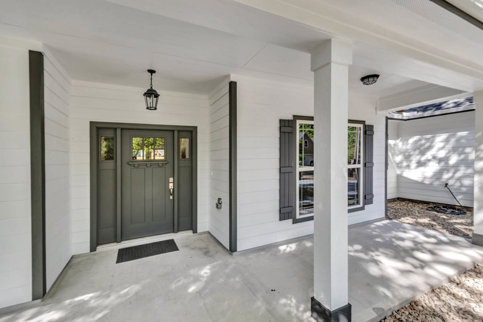 White siding house with grey front door, covered porch with white columns, outdoor lamp fixture, concrete steps, and landscaped entry.