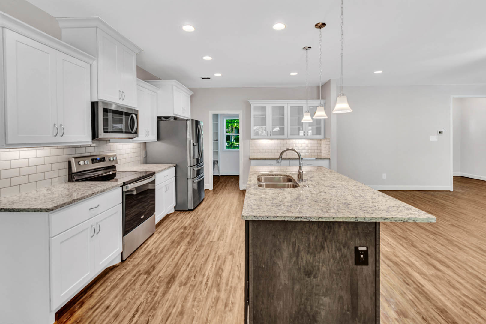 White cabinetry and granite countertops in a kitchen with stainless steel refrigerator, built-in microwave, kitchen island featuring a sink, and visible wall outlet
