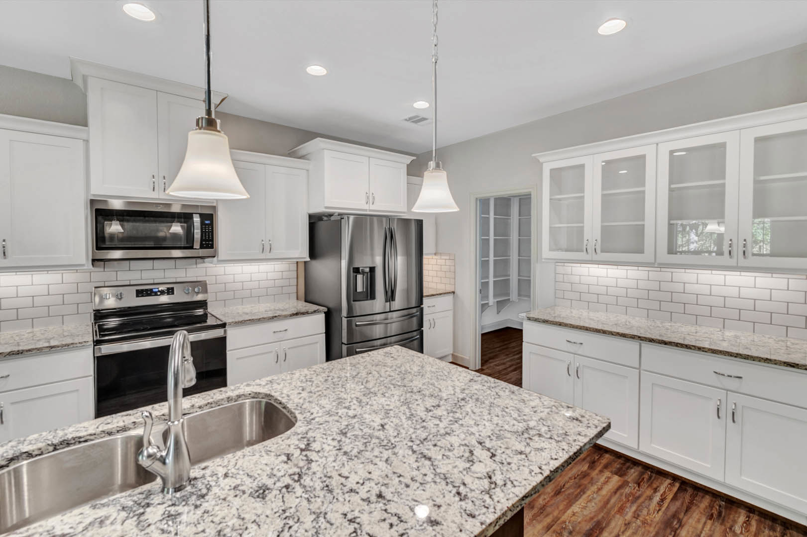 White kitchen cabinets, granite countertops, stainless steel refrigerator and stove, undermount sink with chrome faucet, light-colored backsplash, modern appliances