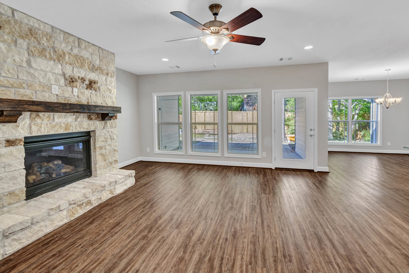 Living room with wood flooring, central fireplace featuring glass doors, ceiling fan with light fixture, white door with window, and large window providing natural light