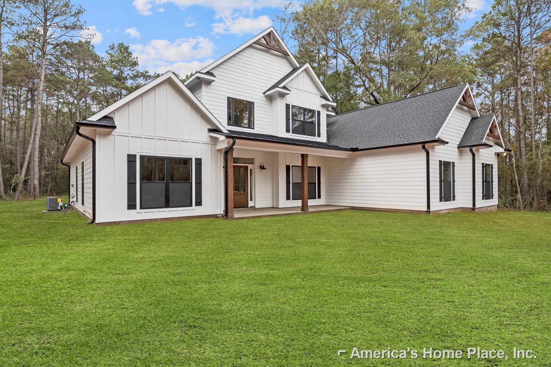 White two-story house with black-framed windows, brown front door and porch posts, green lawn, and tree reflections in glass