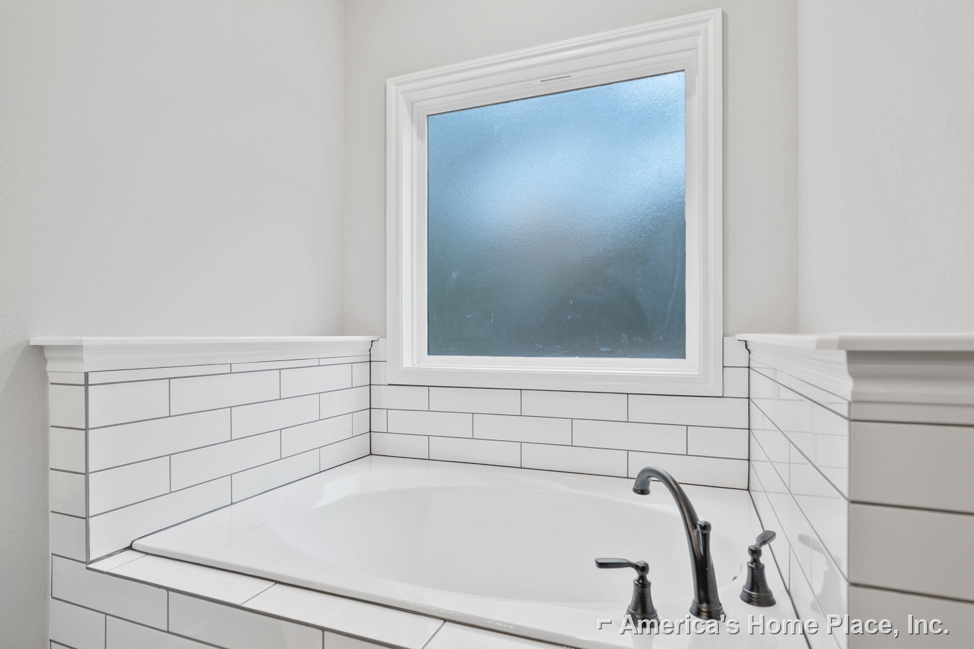 White freestanding bathtub beneath frosted window with blue sky, surrounded by light tile walls and chrome plumbing fixtures in modern bathroom.