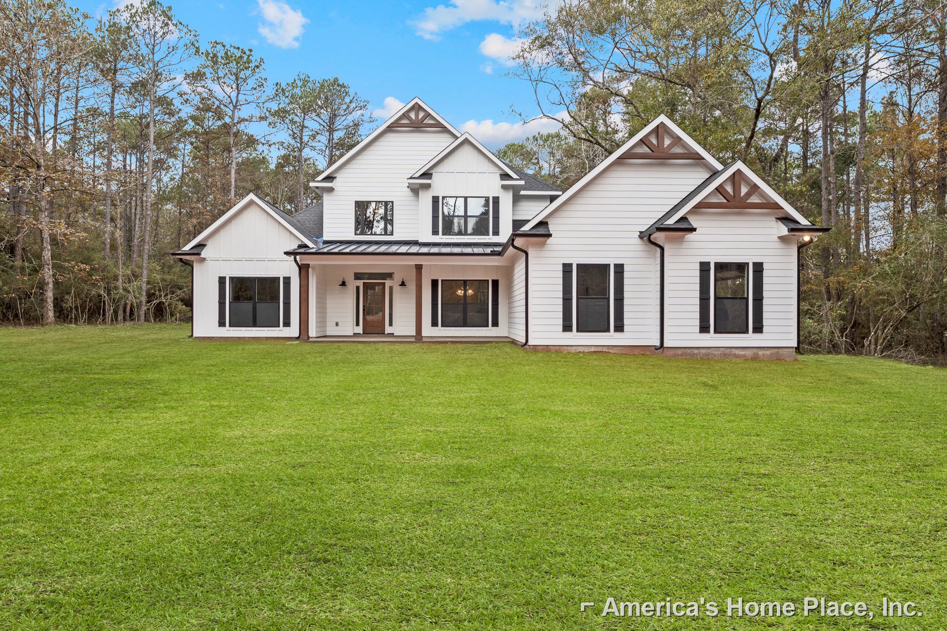 Large white farmhouse with black roof and shutters, manicured green lawn in foreground, Robert Frost Farm visible in background, windows and front door accented by black trim