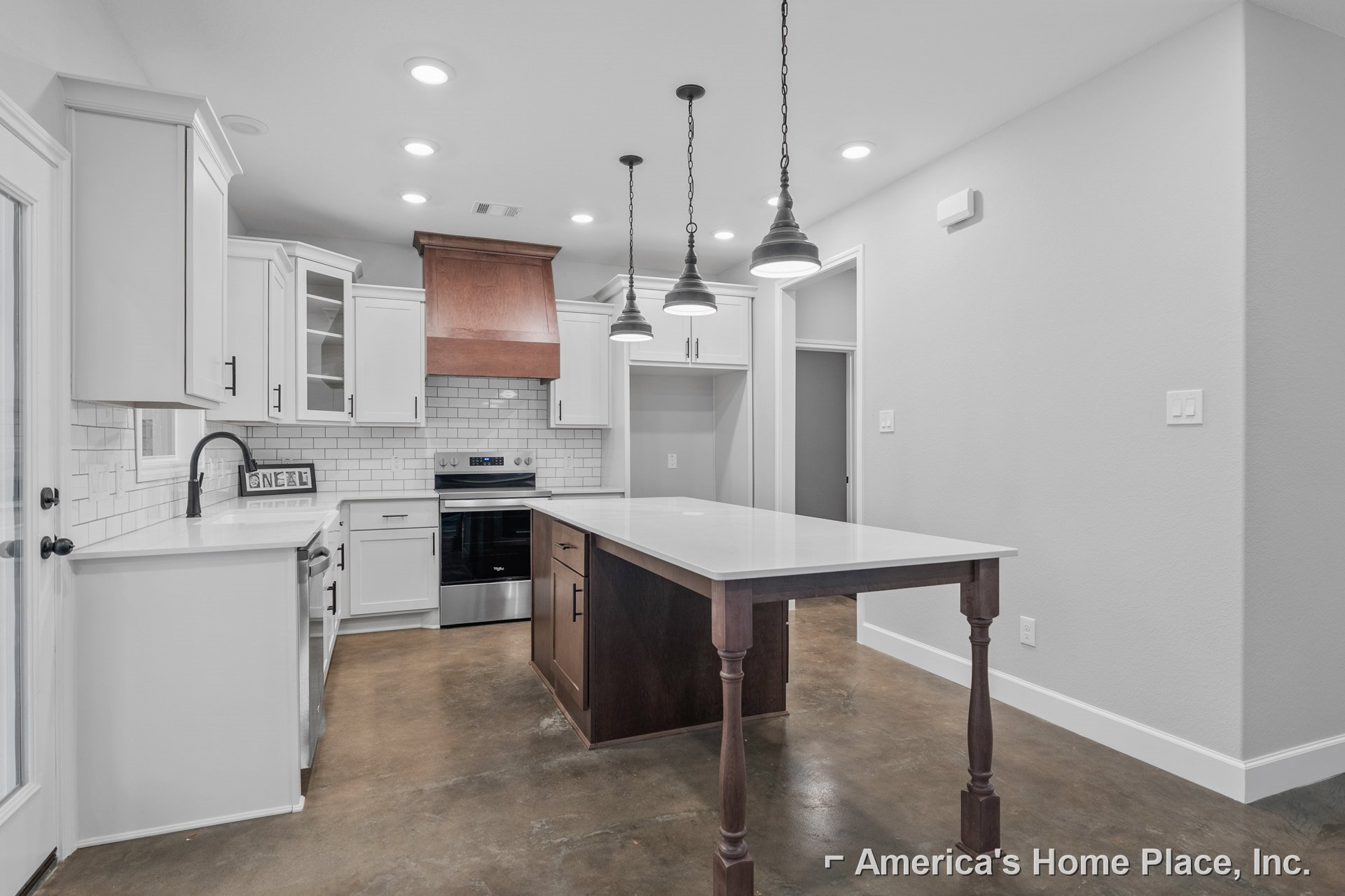 Spacious kitchen featuring a large central island with white countertop and wooden base, stainless steel stove and oven, white cabinetry, modern light fixtures suspended by metal