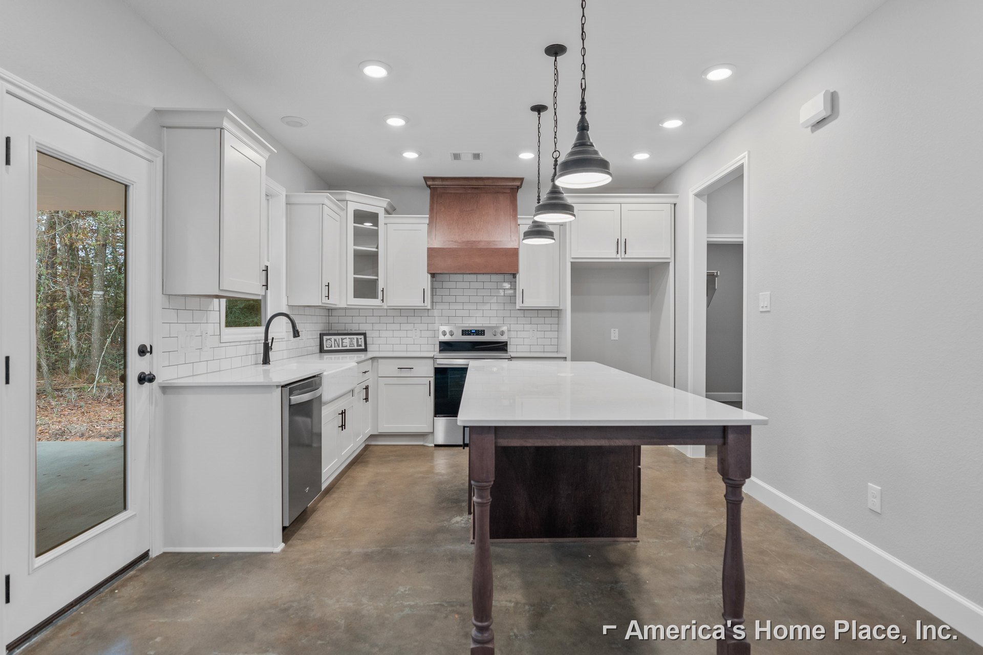 White kitchen with shaker cabinets, subway tile backsplash, black faucet, light wood flooring, and a white dining table near a door overlooking forest scenery