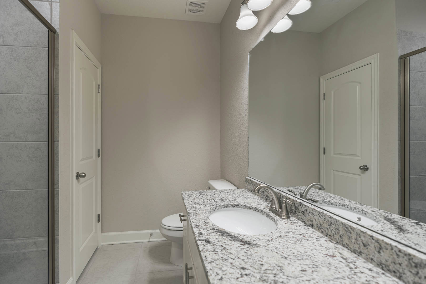 Marble countertop with white vessel sink, large framed mirror above, tile wall, white door with silver handle, recessed ceiling lights