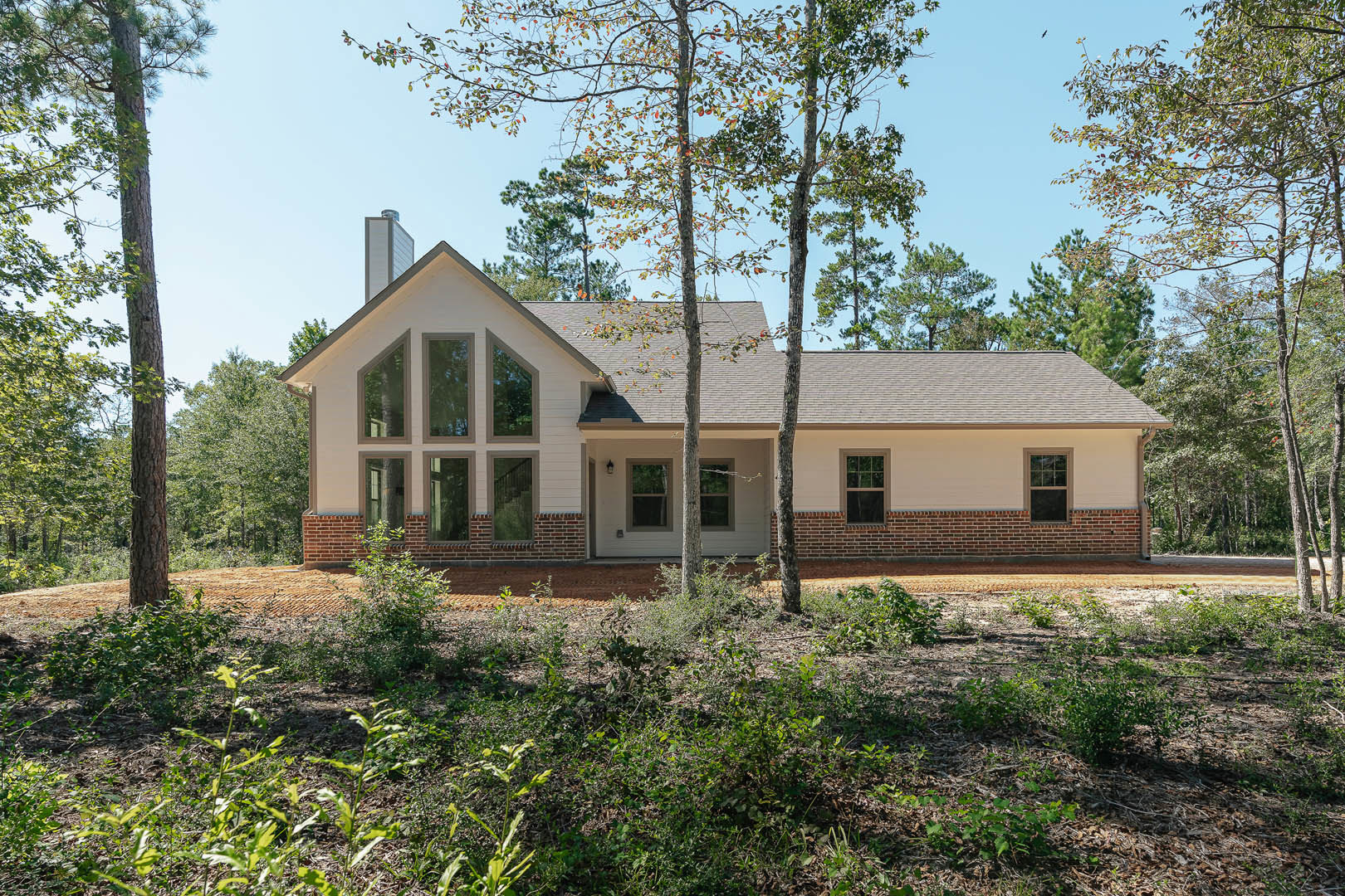 Two-story home with white and black framed windows, surrounded by green bushes and mature trees, front porch partially visible