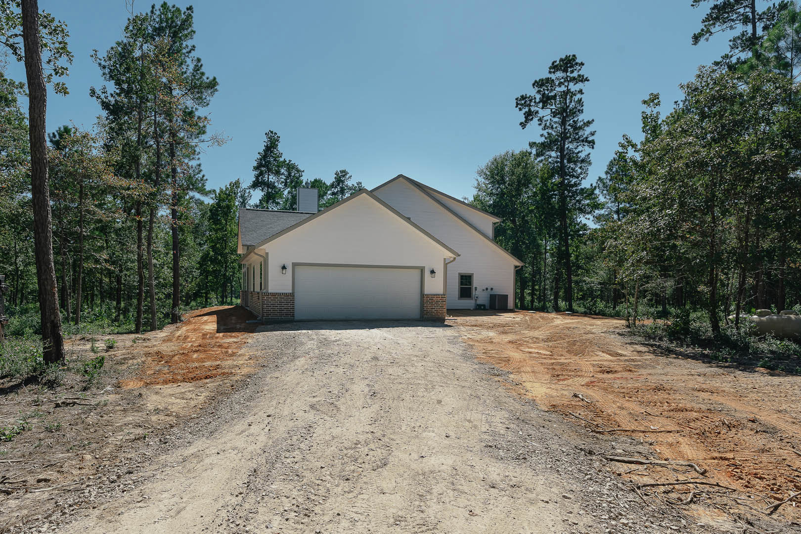 Modern cottage-style home with white exterior walls, attached garage, paved driveway, mature trees with leafy canopies, and landscaped front yard.