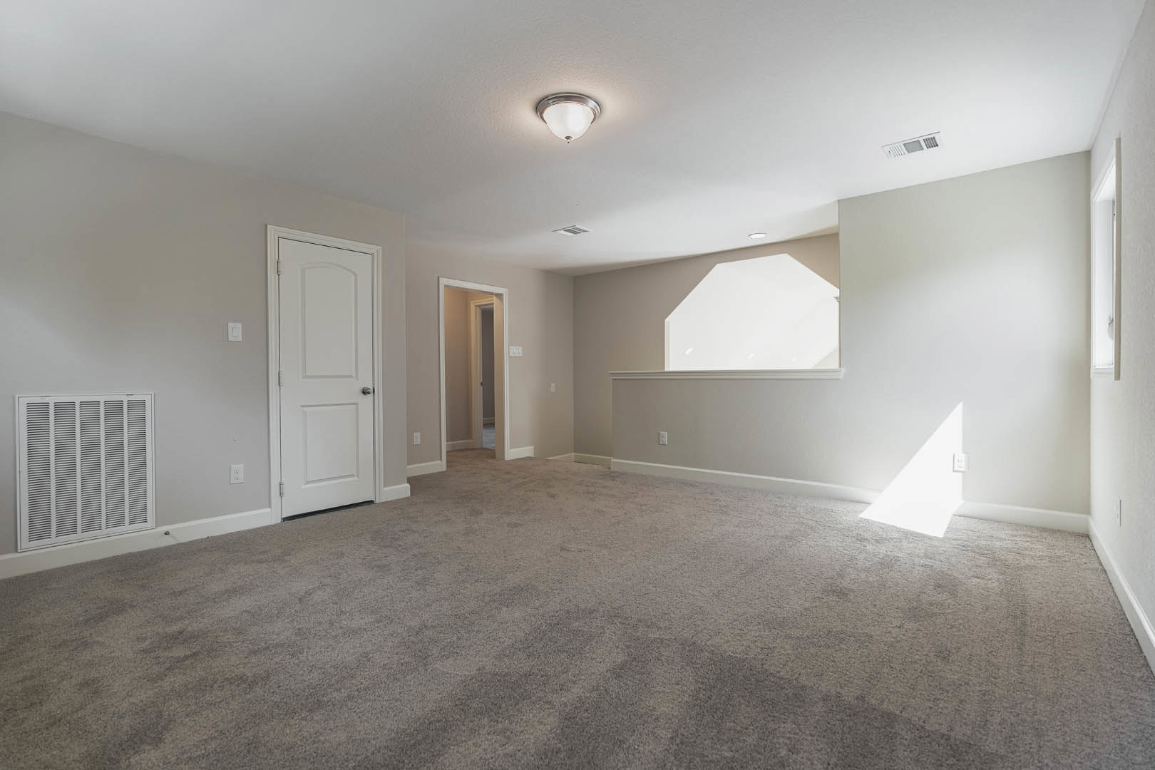 Carpeted room with white walls, white door featuring a silver handle, rectangular window, ceiling light fixture, and a close-up of a vent.