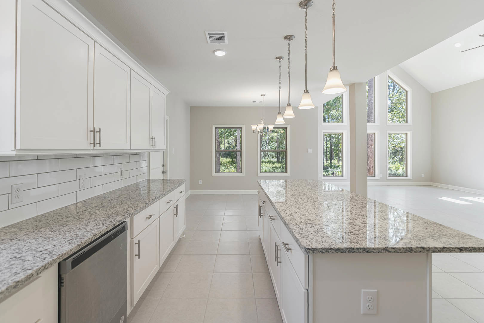 White kitchen cabinets with granite countertops, stainless steel dishwasher, tile backsplash, marble counter detail, ceiling vent, wall outlet, and window overlooking trees.