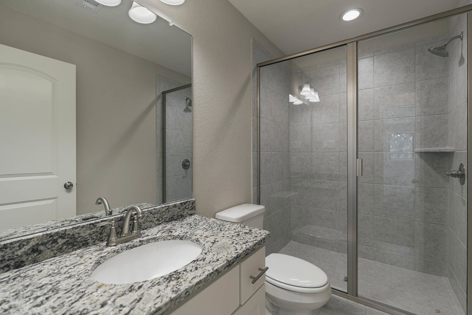 Modern bathroom featuring a glass-enclosed shower, white porcelain sink with chrome faucet, wall-mounted mirror, closed toilet, recessed ceiling light, and smooth white tile walls