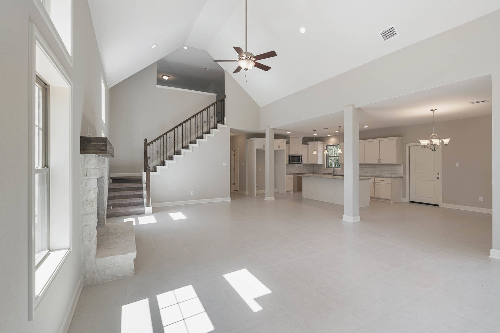 Spacious white interior featuring a staircase with wooden steps, white walls, ceiling fan with light fixture, white door with silver handle, and light-colored flooring illuminated