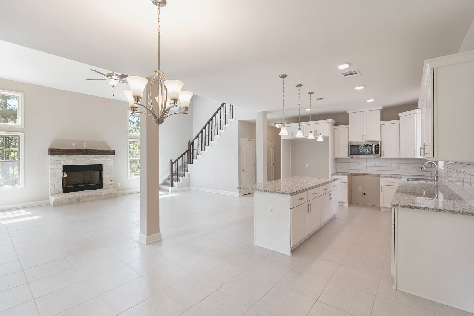 Spacious open-plan kitchen and living room with white cabinetry, granite kitchen island, stainless steel microwave, tiled floors, fireplace featuring a white centerpiece