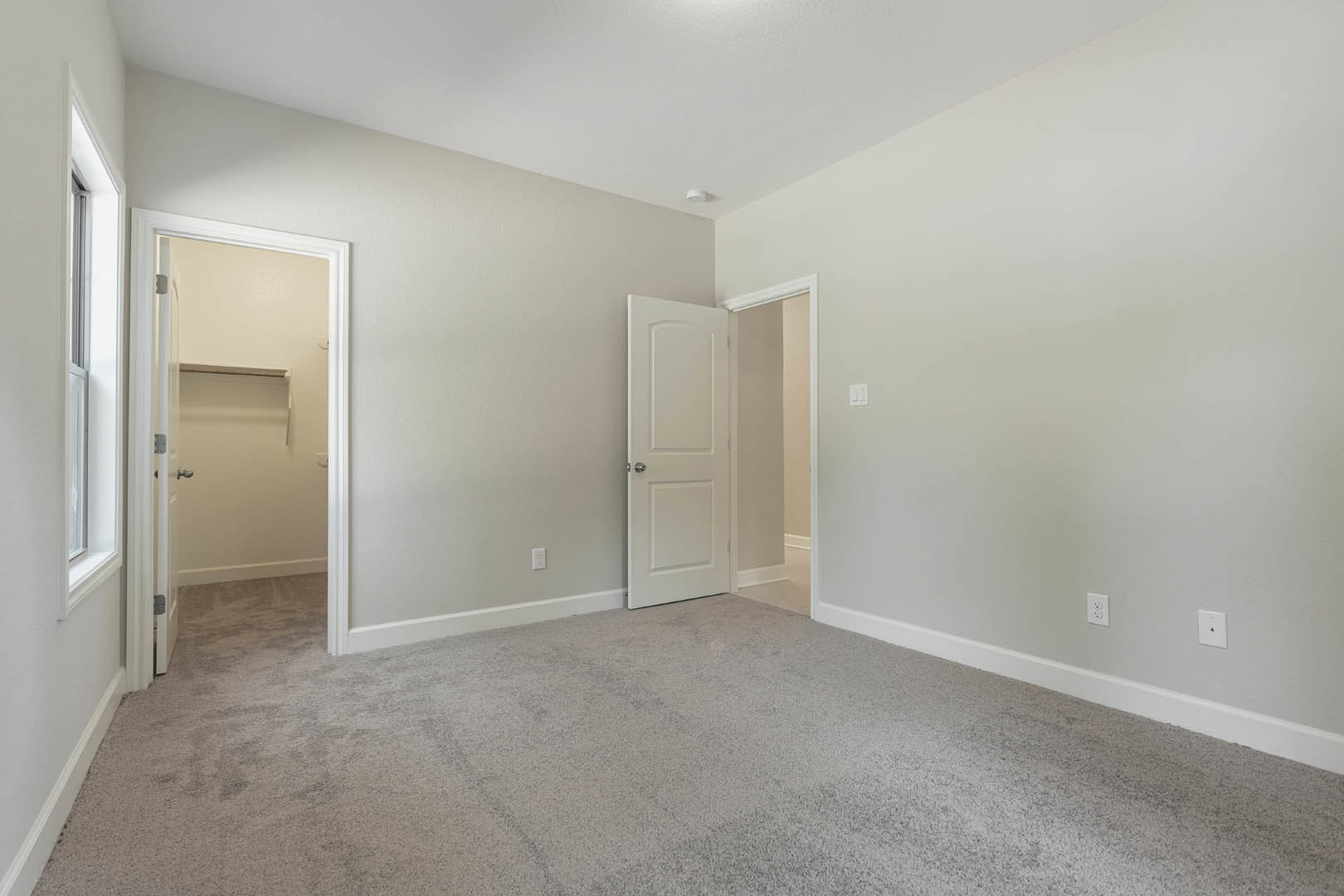 White door with silver knob open to a closet, carpeted floor and walls, white trim and molding, soft neutral finishes throughout the room