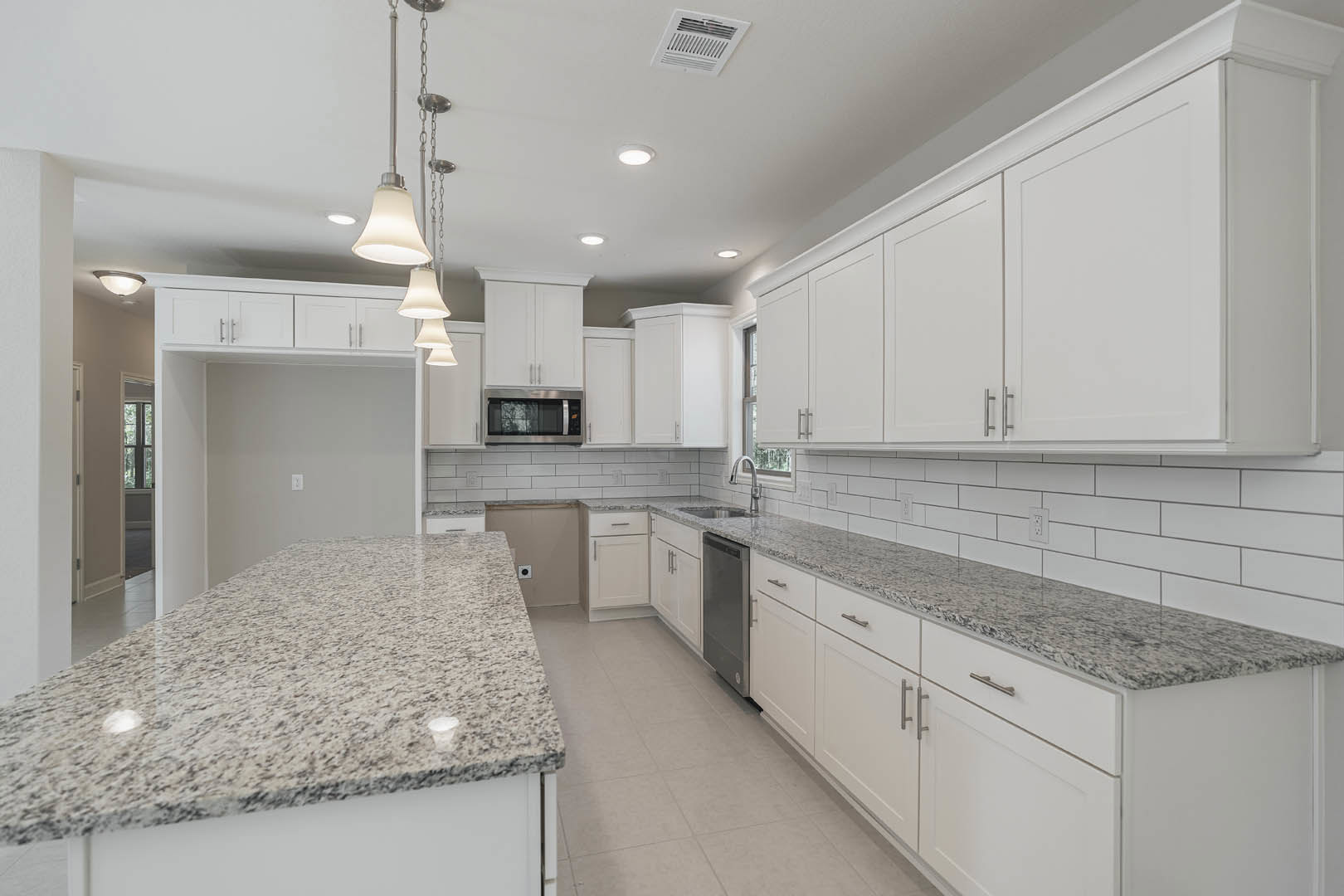 White kitchen with granite countertops, silver cabinet handles, black-framed window, white wall vent, and stainless steel appliances.